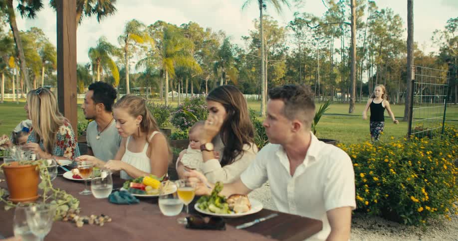 A girl runs through a park to join her family and friends at a picnic table