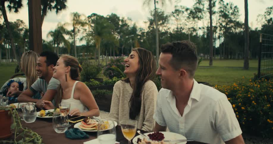 A group of friends and family laugh while eating a meal in a park