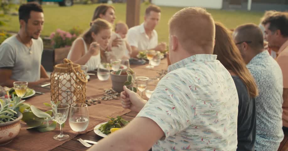 A man sits down at a picnic table for a meal with friends and family