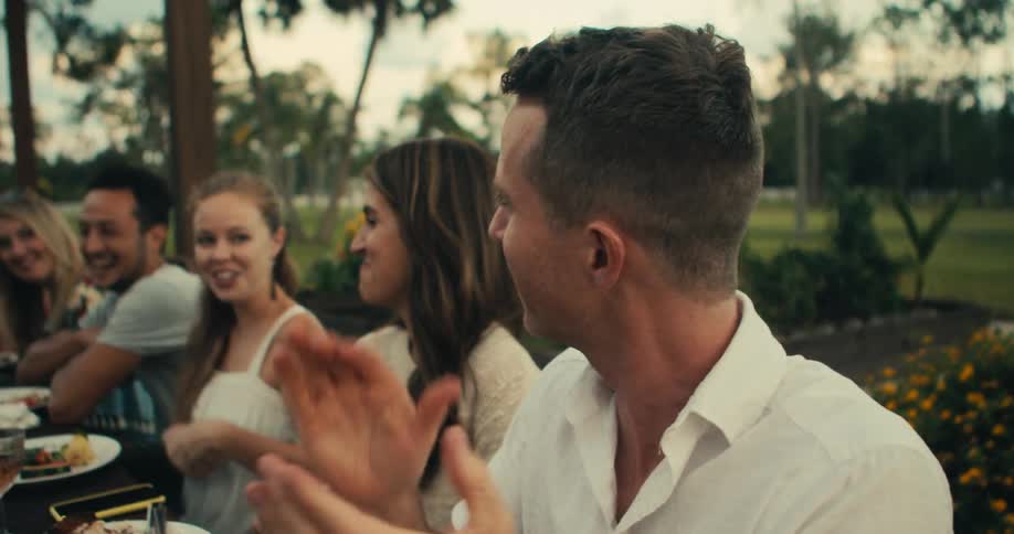 A man starts a clap and cheer at a dinner with friends in a park