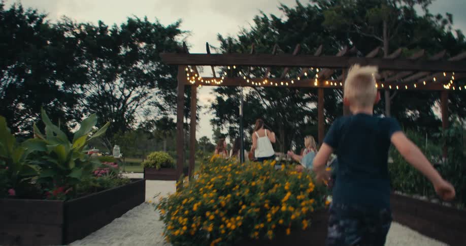 A boy runs toward the dining table under the pergola and fairy lights
