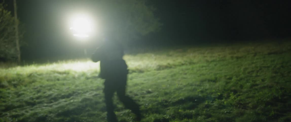 An officer rushes forward down a grass filled hill at night