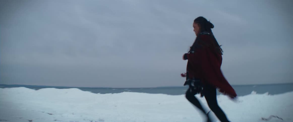A woman wearing a poncho is running through the snow and turns to look behind her