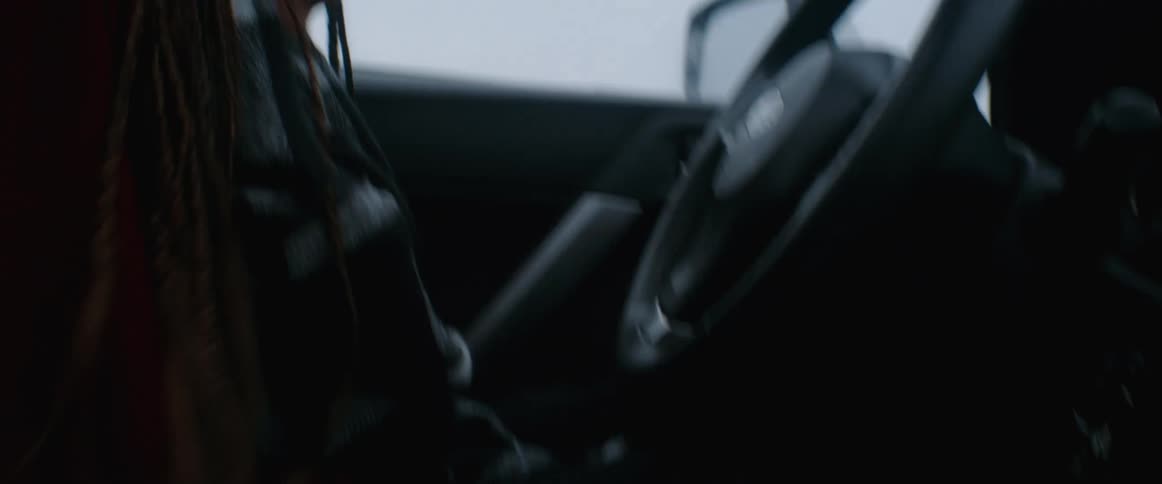 A woman is sitting in parked car and looks cold warming hands