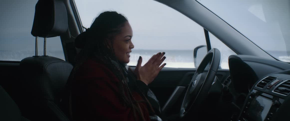 Woman gets into car and rubs her hands together to warm them as snow covers ground nearby