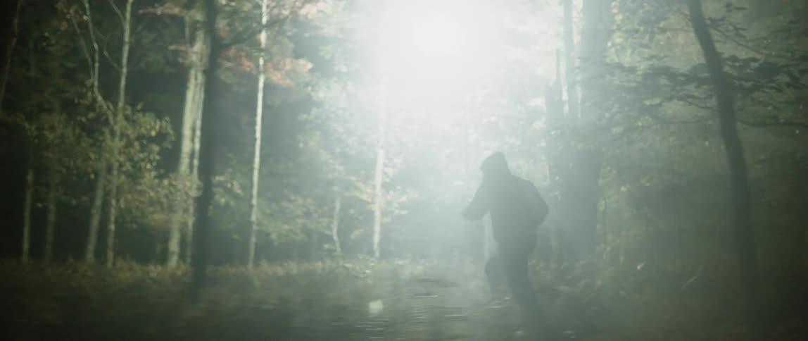 A man races and jumps through a forest as a spotlight follows him
