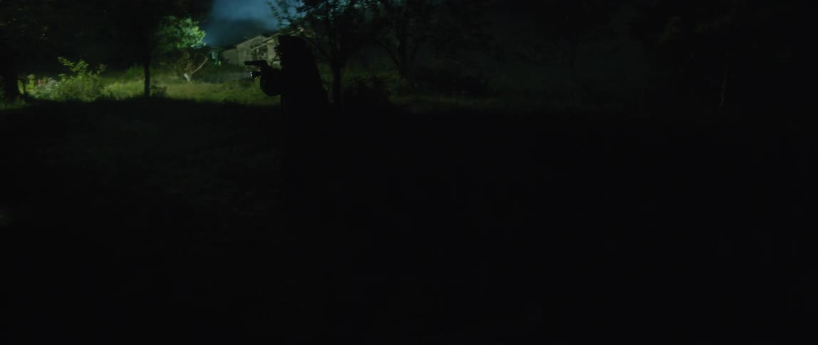 An officer is moving over a grass field at night with gun drawn