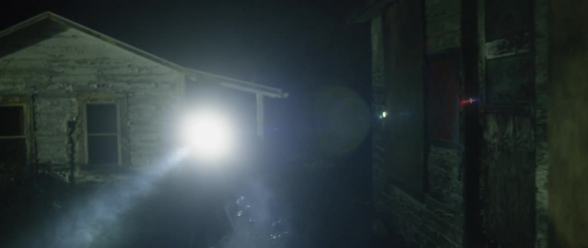 An officer is walking around homes at night with a flashlight and gun