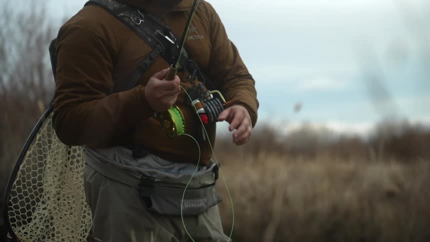 A man fishing in a river pulls his rod back