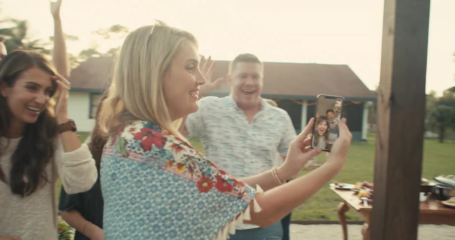 Friends greet friend on video call as woman walks phone around backyard party