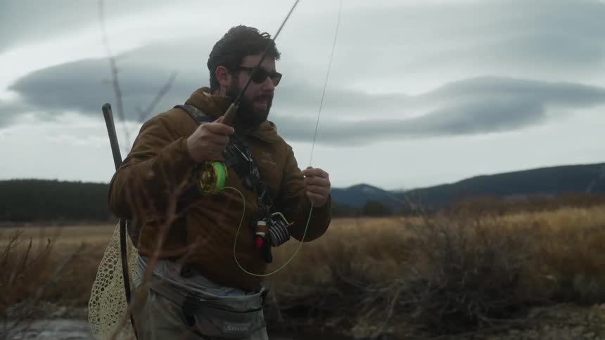 A man with sunglasses casts his fishing line into the river
