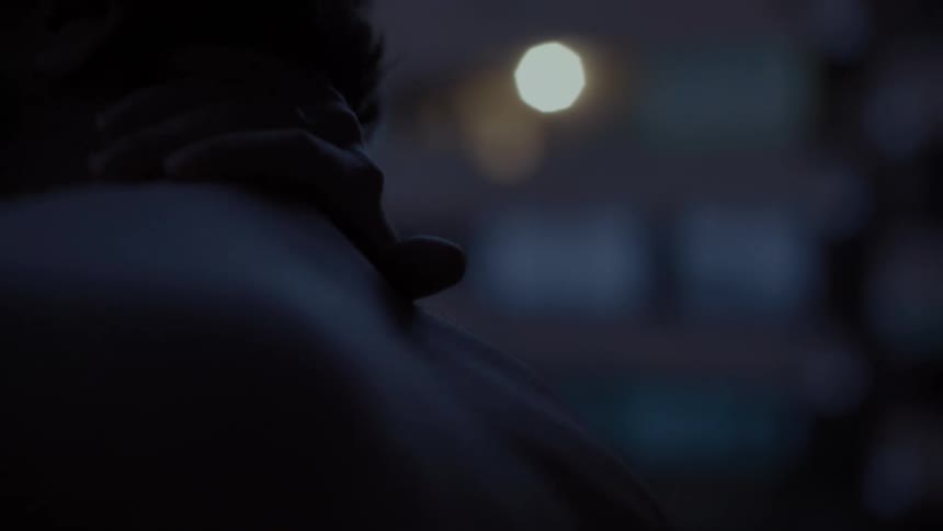 Man with curly hair rubs his neck in front of apartment buildings