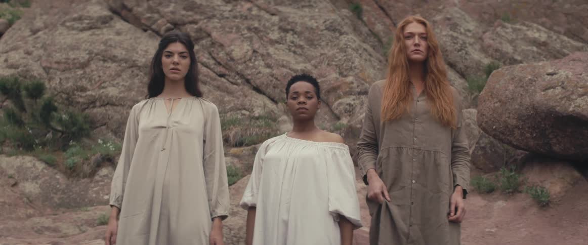 Three women in the wilderness slowly step towards the camera