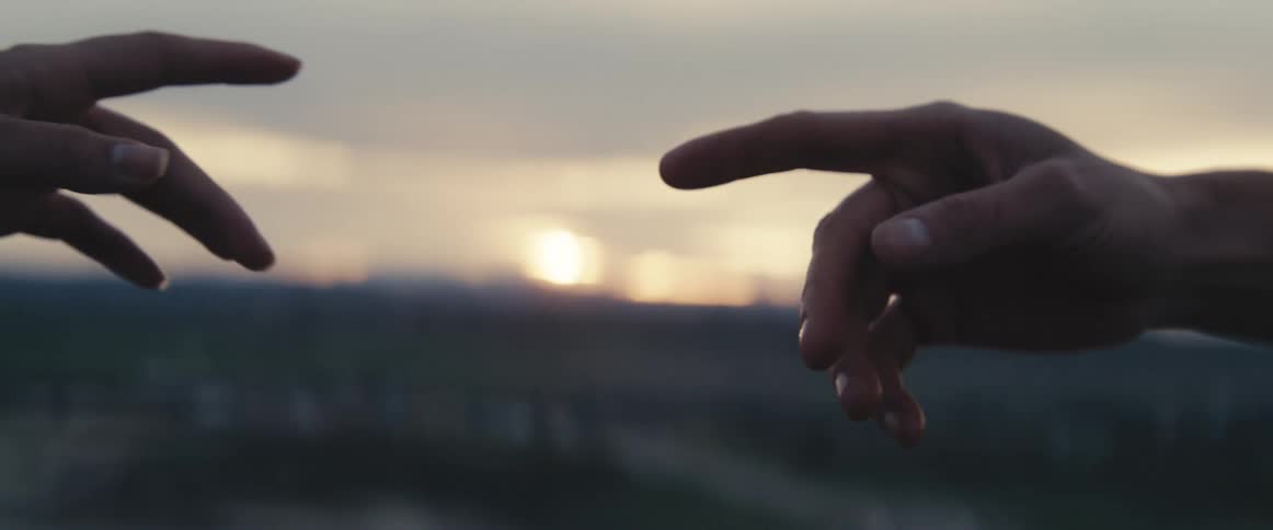 Woman and man reach hands out to touch fingers as sun sits on horizon