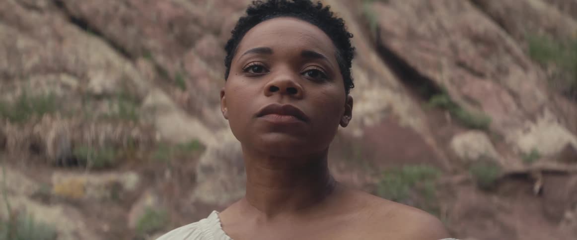 A black woman is standing outside with a mountain behind her