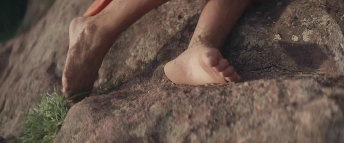 A woman with dirt all over her legs leans against the side of a cliff