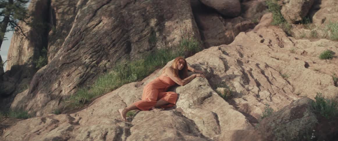 Woman reclines on boulders at base of mountain slope
