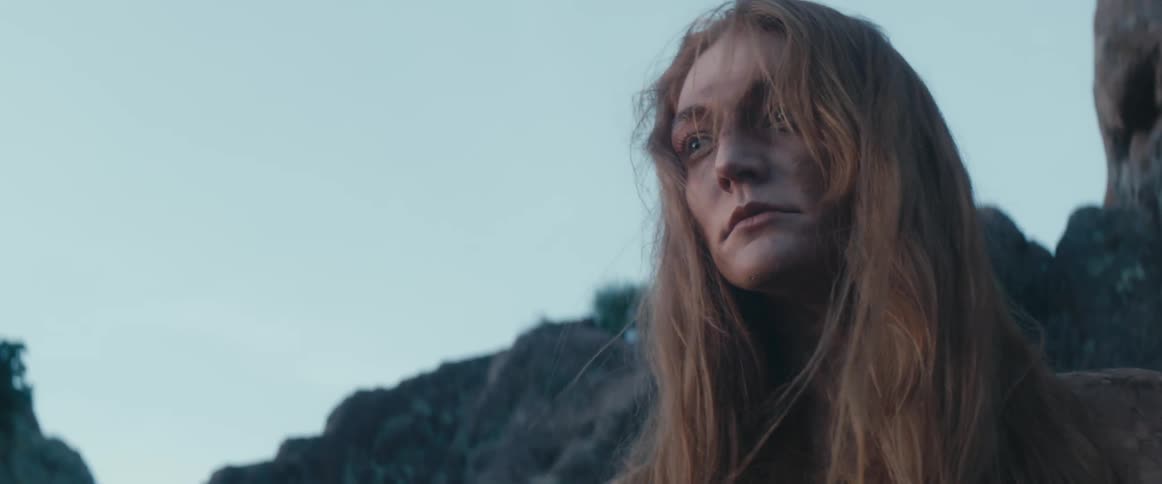 A woman with long red hair is standing outside as the wind blows her hair