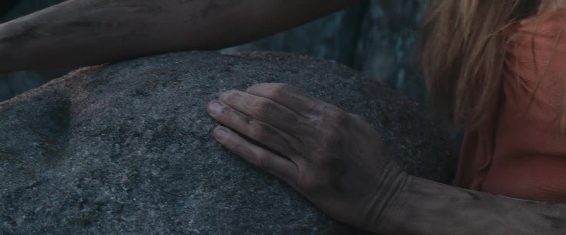 Woman leans against rock outdoors as dirt coats her skin