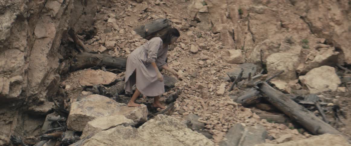 Woman walks barefoot across debris of landslide and stoops to pick something up