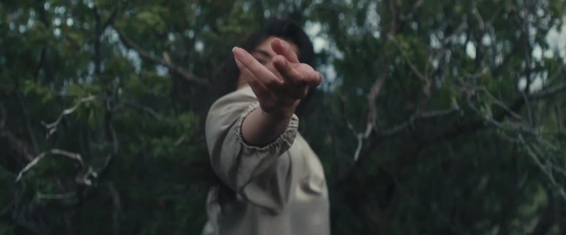 A woman reaches out her arm and hand as she stands in a forest