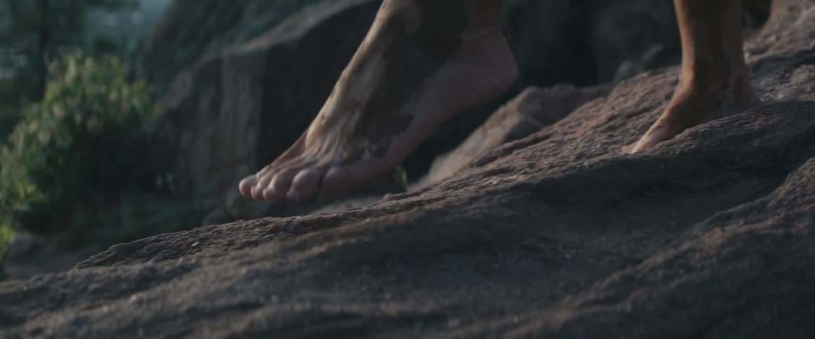 Person wearing peach pants walks barefoot across stone slope