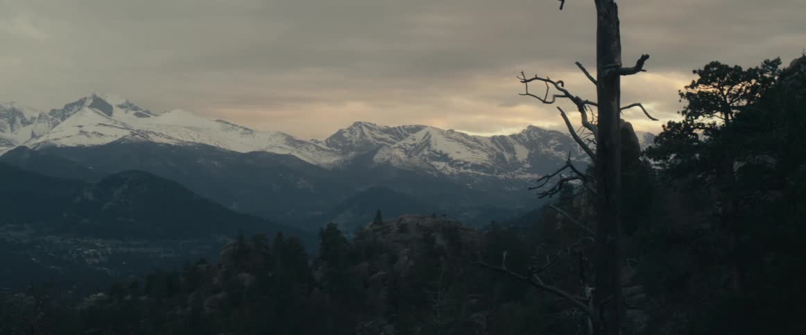 A snowy mountain range looms over the countryside on a cloudy day