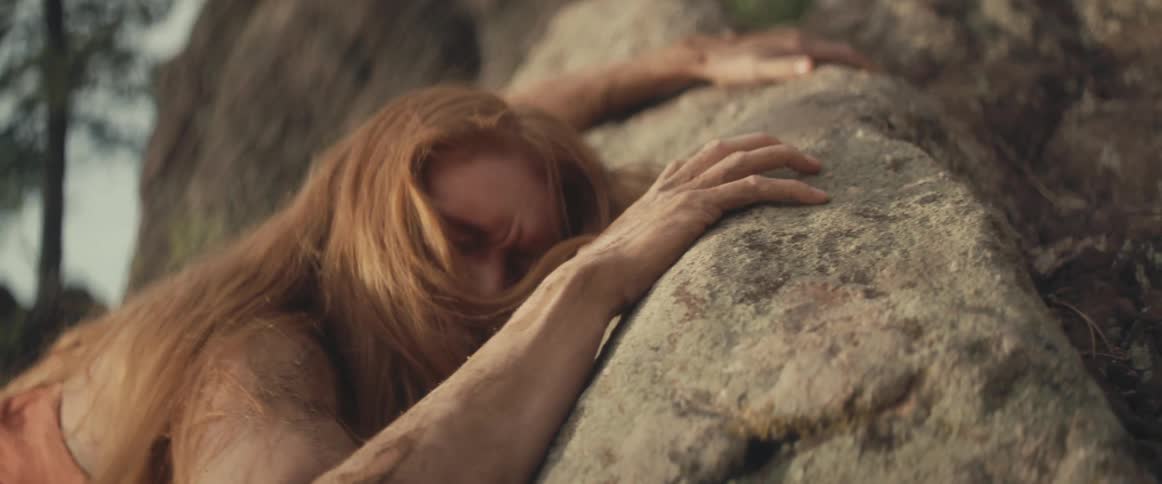 A woman covered in dirt cries while lying outside on large rocks