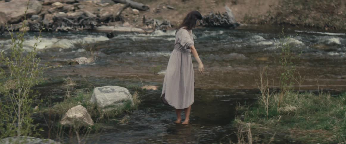 A woman in a dress leans down into the water and then spins around