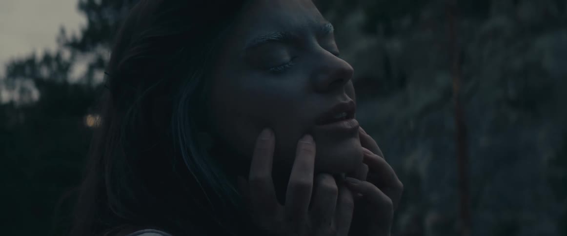 Woman touches her green painted face in the woods