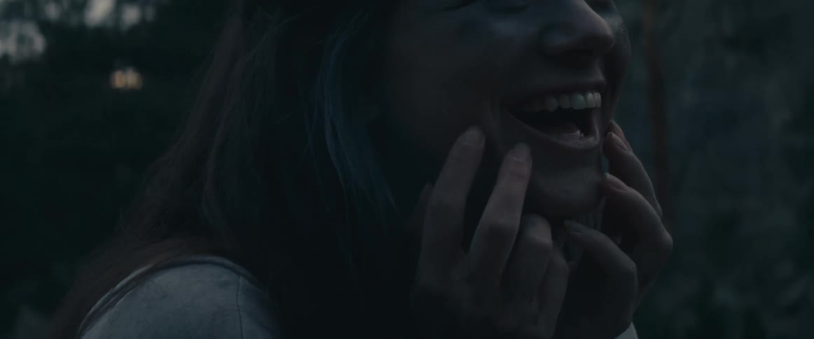 Woman with straight hair white dress scratches her green face in rocky hill laughing