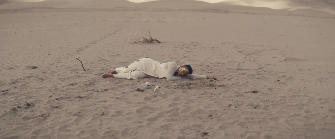 A black woman wearing white clothes is sleeping on the desert sand