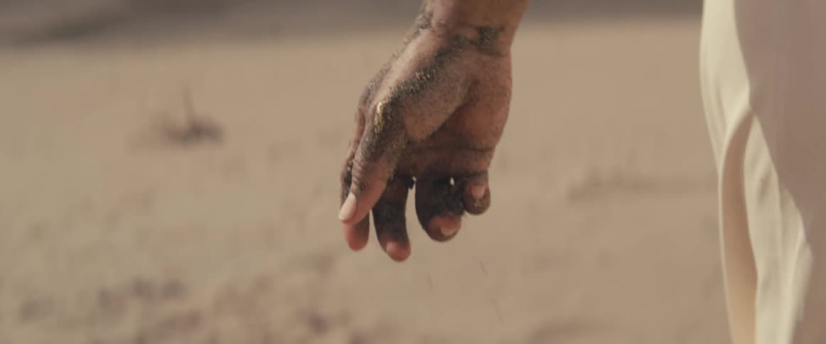 A person dropping an item in the sand outdoors