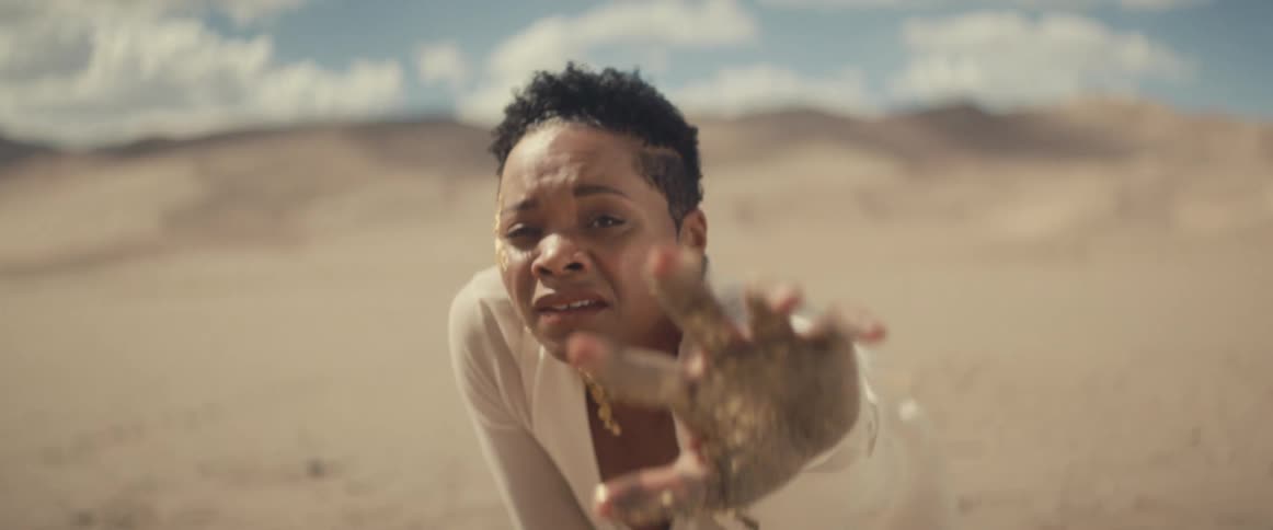 A woman crawling through the desert and reaching out