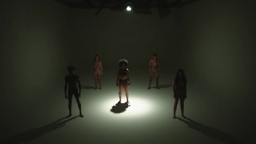 Five people stand in a white room in their underwear as a light strobes overhead