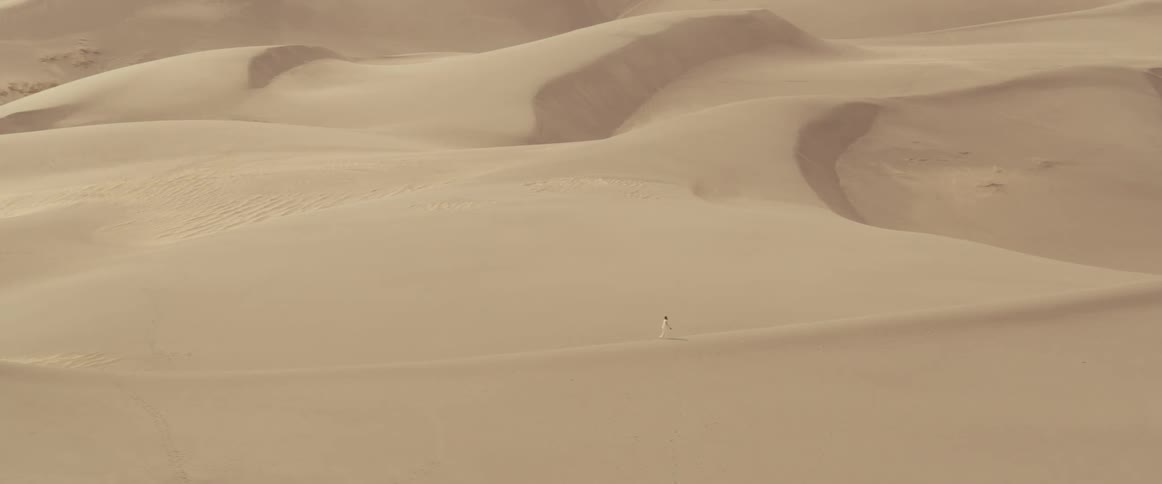 A person walks across a sand dune in a vast desert during the day