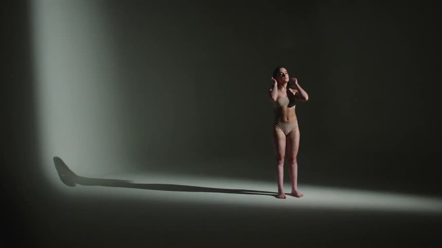 A woman wearing underwear is standing in a dark room as a light flashes