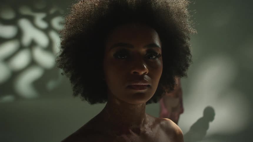 Female model with curly hair stands facing the camera in front of male and female models in the studio