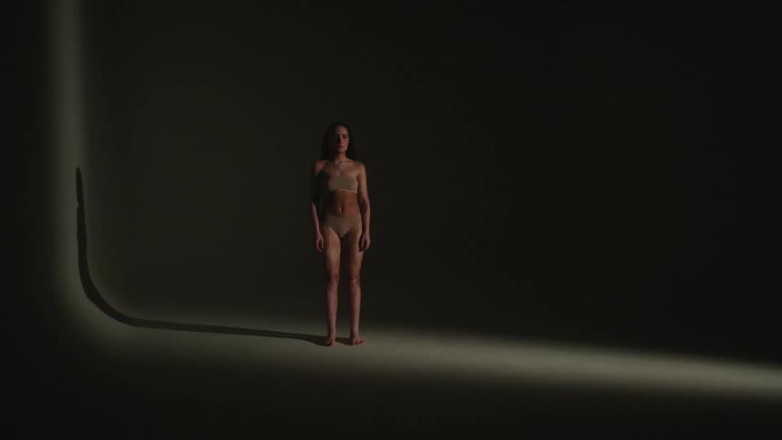 A woman stands in an empty room in her under garments as a light flashes on and off