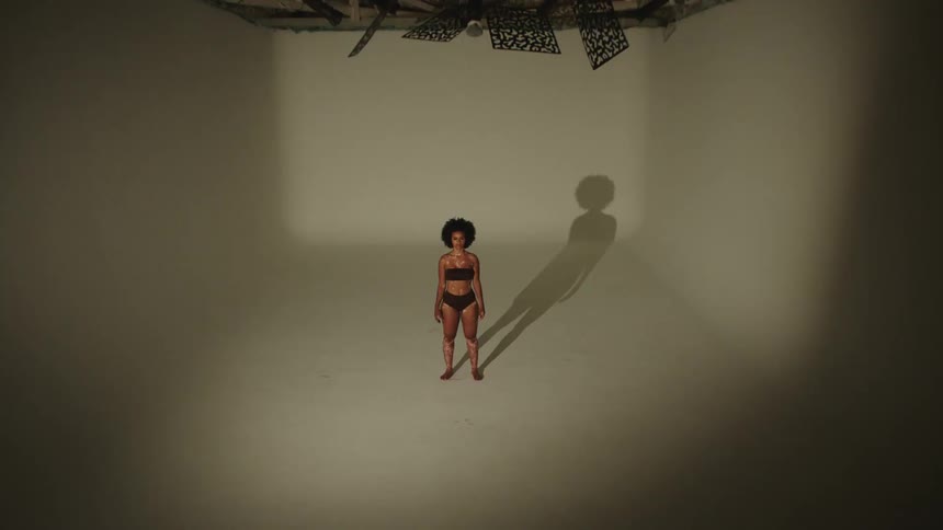 Woman stands in white room as light flashes on and off wearing underwear