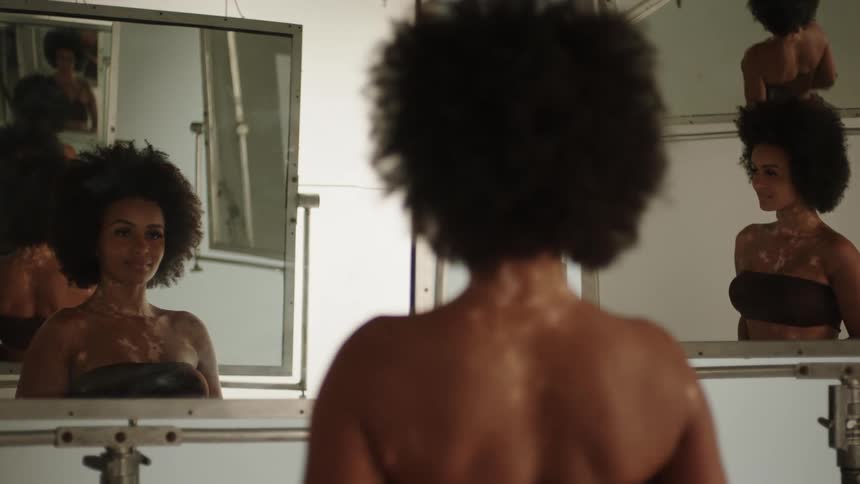 Woman wearing strapless bra stands in front of a series of mirrors that reflect her and over and over