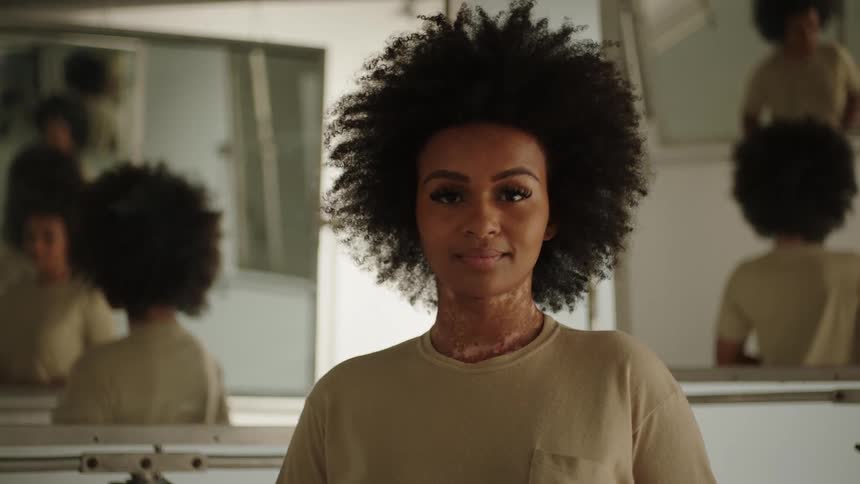 A woman stands in a room with two mirrors behind her and smiles