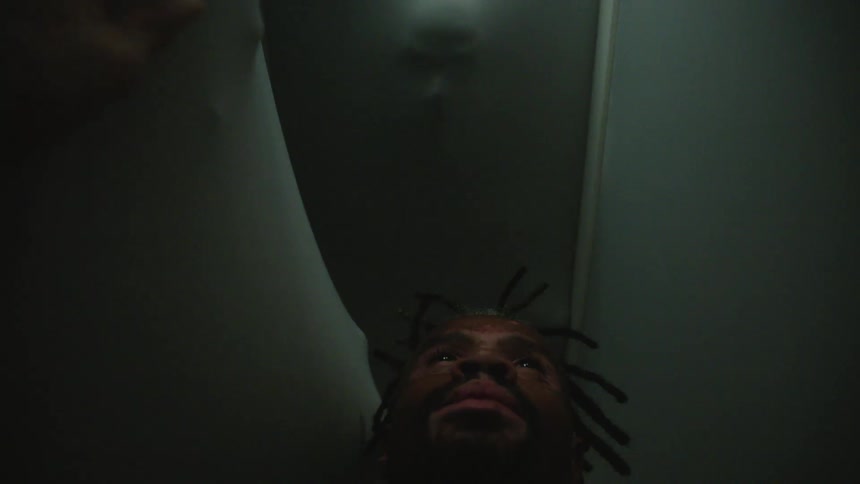 A man floats in a narrow dark hallway as hands from the other side reach towards him