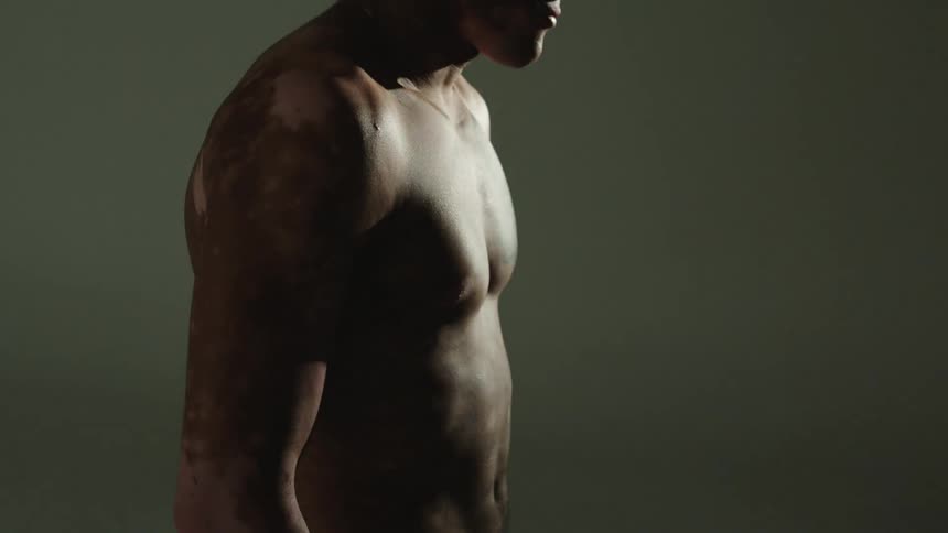 A man with patches on his bare chest stands in a white room with a strobing light