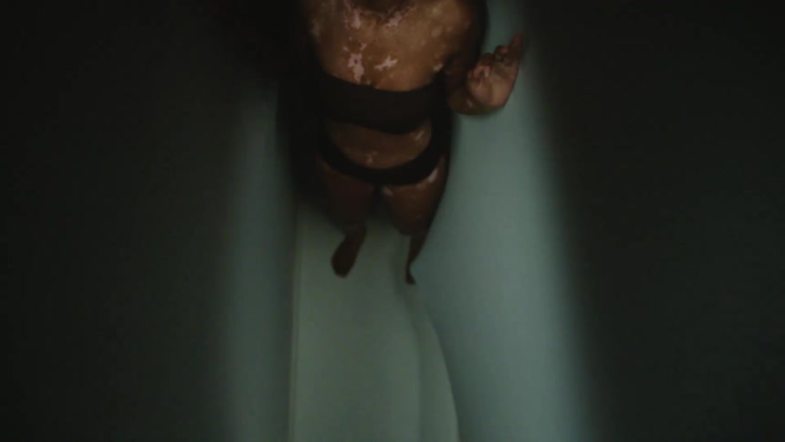 A fearful young woman tries to cover her body and moves backwards as she stands in a small space with hands on the other side of the soft wall reaching for her
