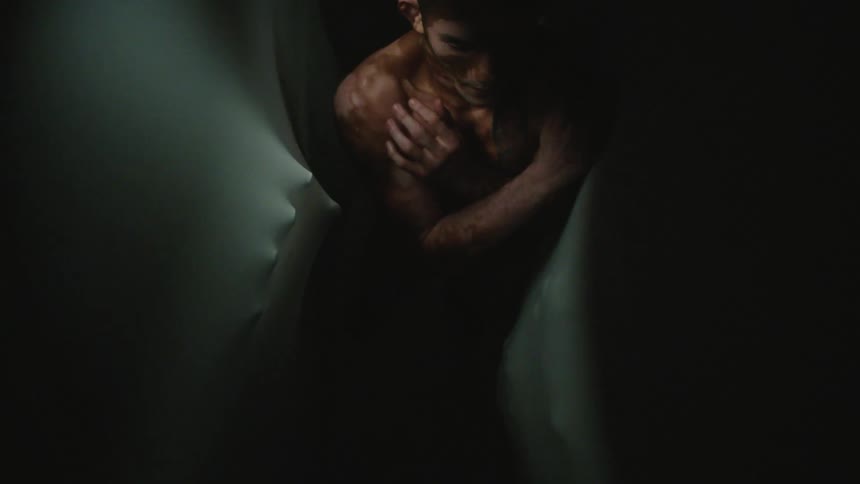 A shirtless man is scared as people reach around him from behind stretchy fabric walls