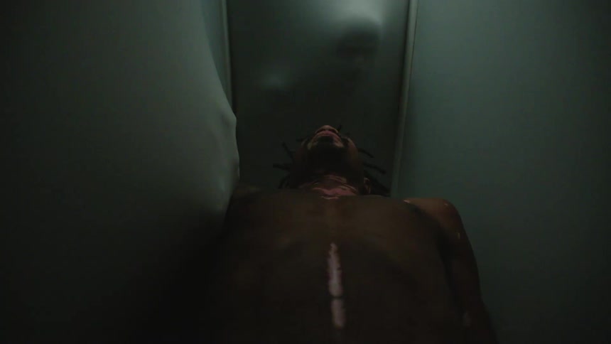 A man lays in a small room as the walls stretch with peoples faces