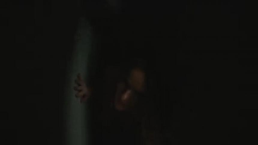 A woman crawls on the floor of the dark room
