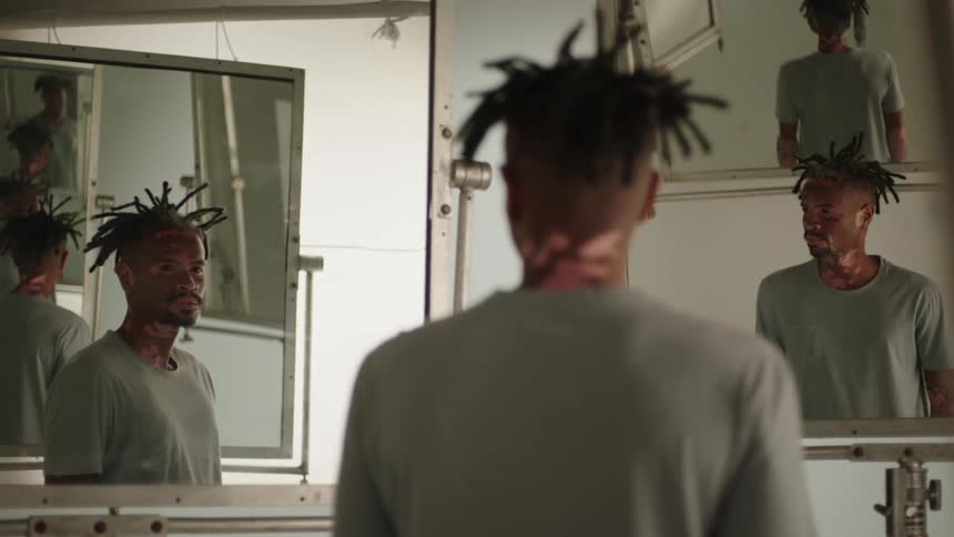 A man stands and looks in a mirror and then turns and looks in another mirror and then turns around