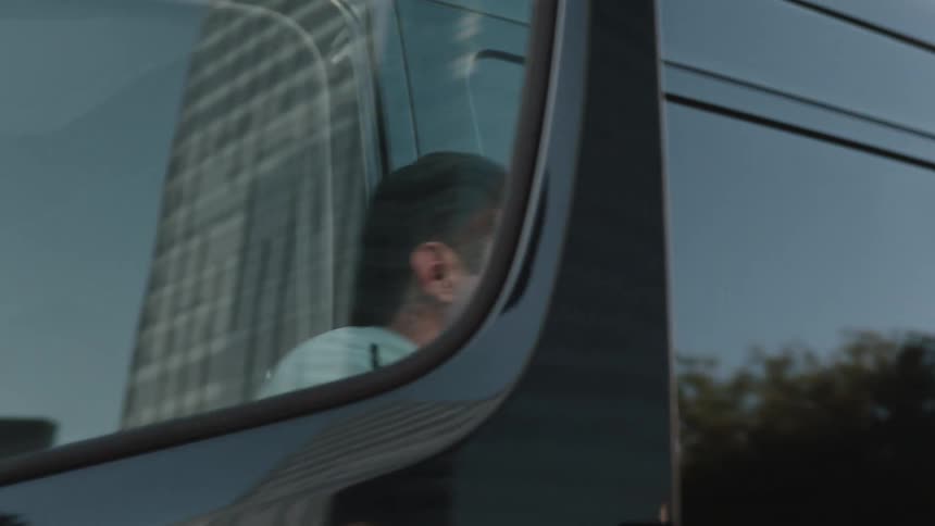A man gets out of a black transport van with large tinted windows that reflect the surrounding buildings downtown